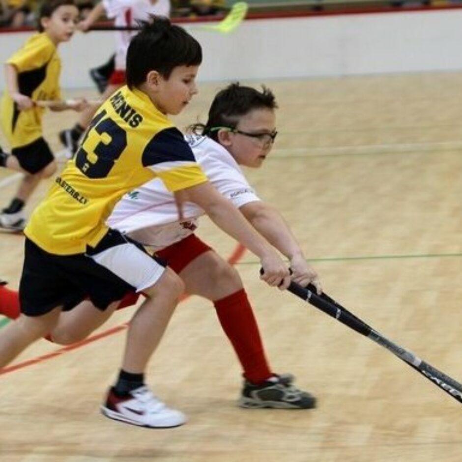 Divi zēni sporta tērpos spēlē florbolu