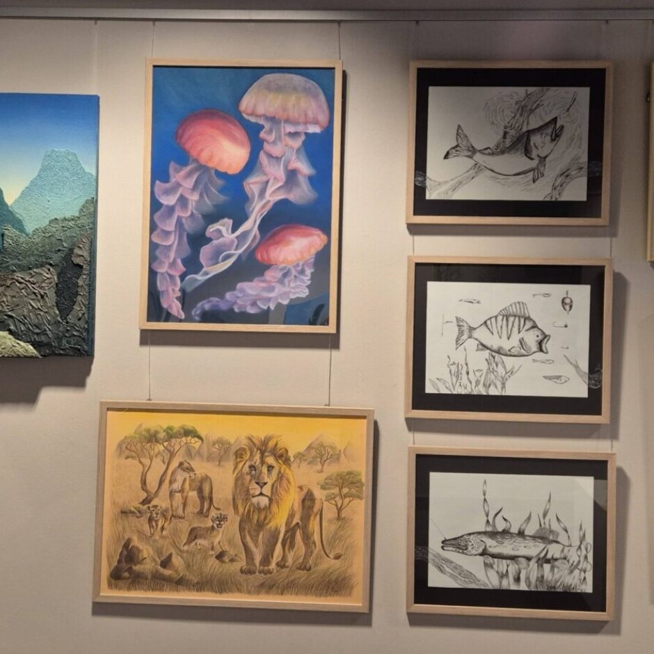 Pie sienas pakārti dažādi gleznojumi un zīmējumi, tostarp medūzu, zivju, Āfrikas savannas ainavas, modernas arhitektūras un stilizētu ciematu attēli, kā arī trīsdimensiju kalnu ainava.