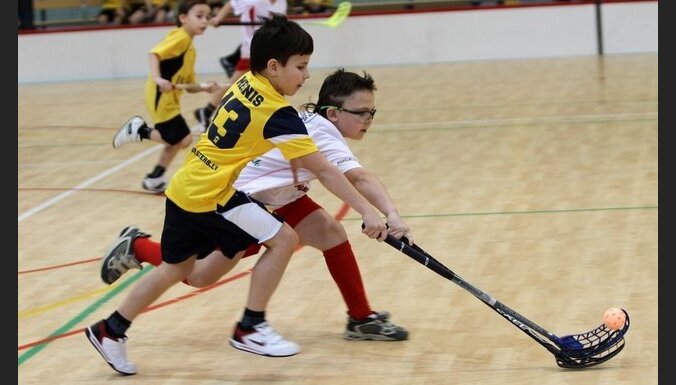 Divi zēni sporta tērpos spēlē florbolu