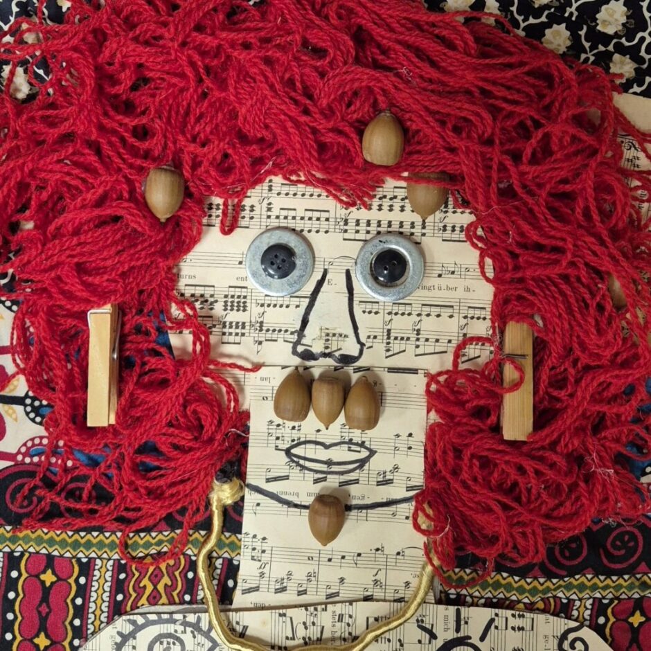 Kolāža ar cilvēka seju, veidota no auduma, pogām, papīru un dabas elementiem.